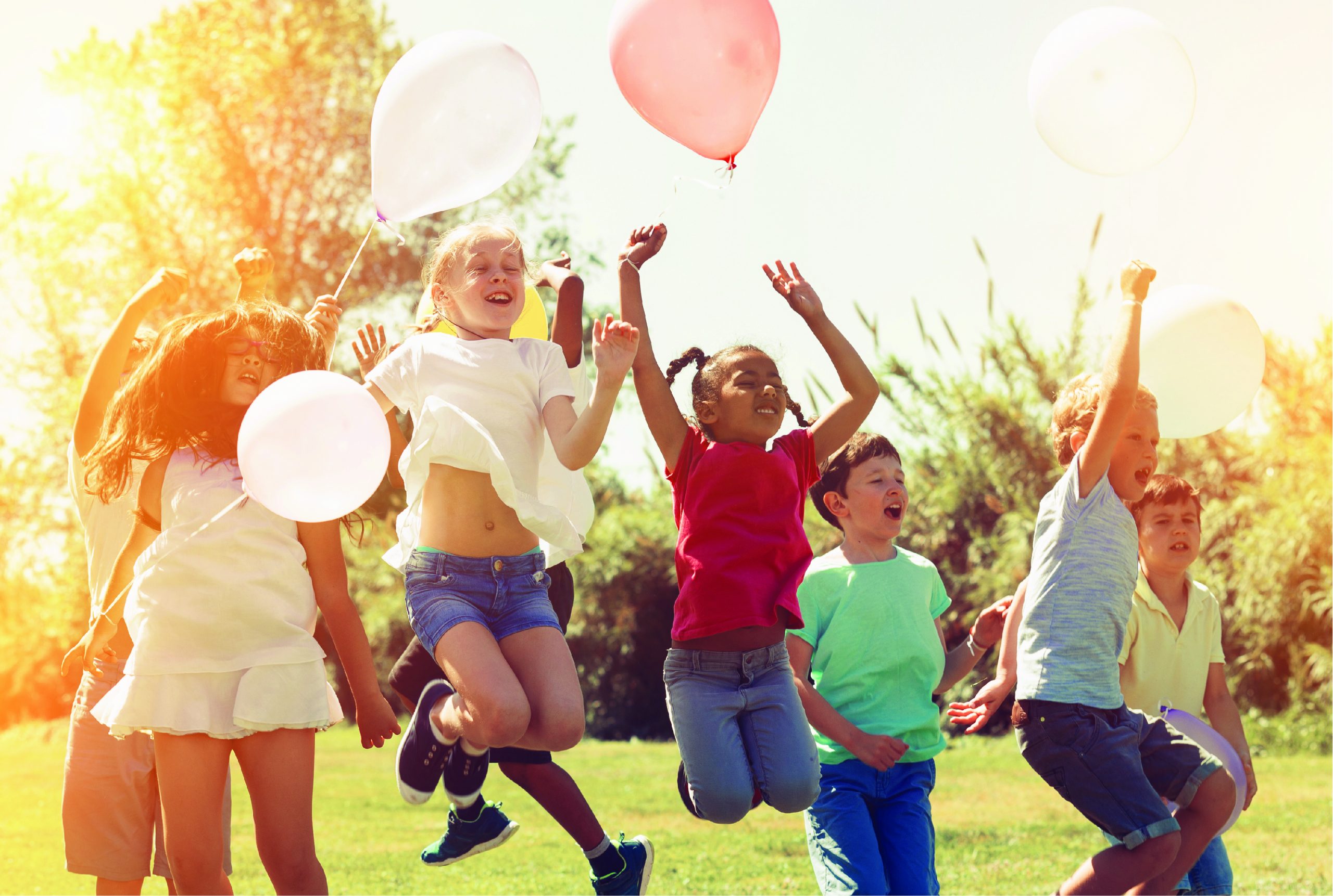 Happy playful children with balloons jumping around outdoors