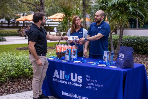 Male and female at All of Us event table passing out informational pamphlet